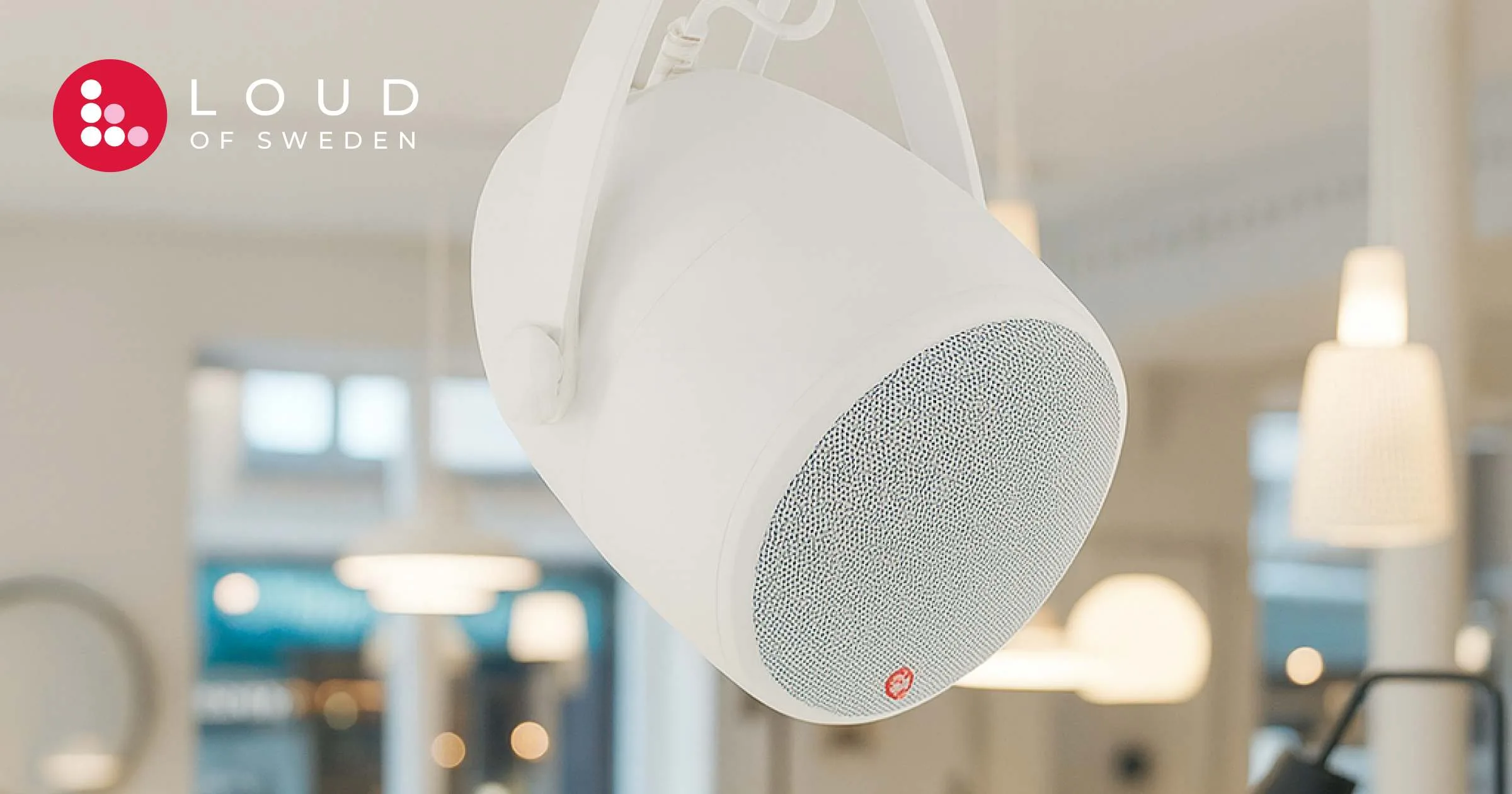 Enceinte de plafond blanche Loud of Sweden suspendue dans un environnement de bureau moderne avec arrière-plan flou.